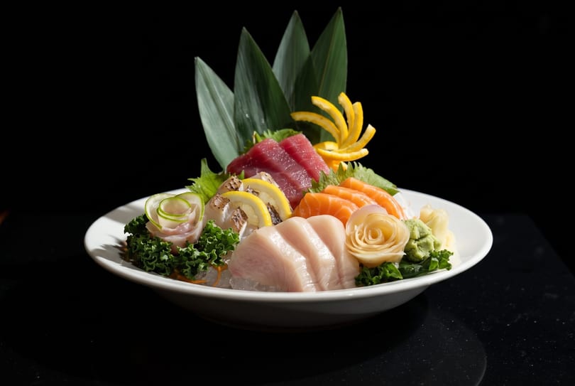 A white platter of assorted sashimi, including tuna, salmon, and white fish, garnished with lemon and greens.