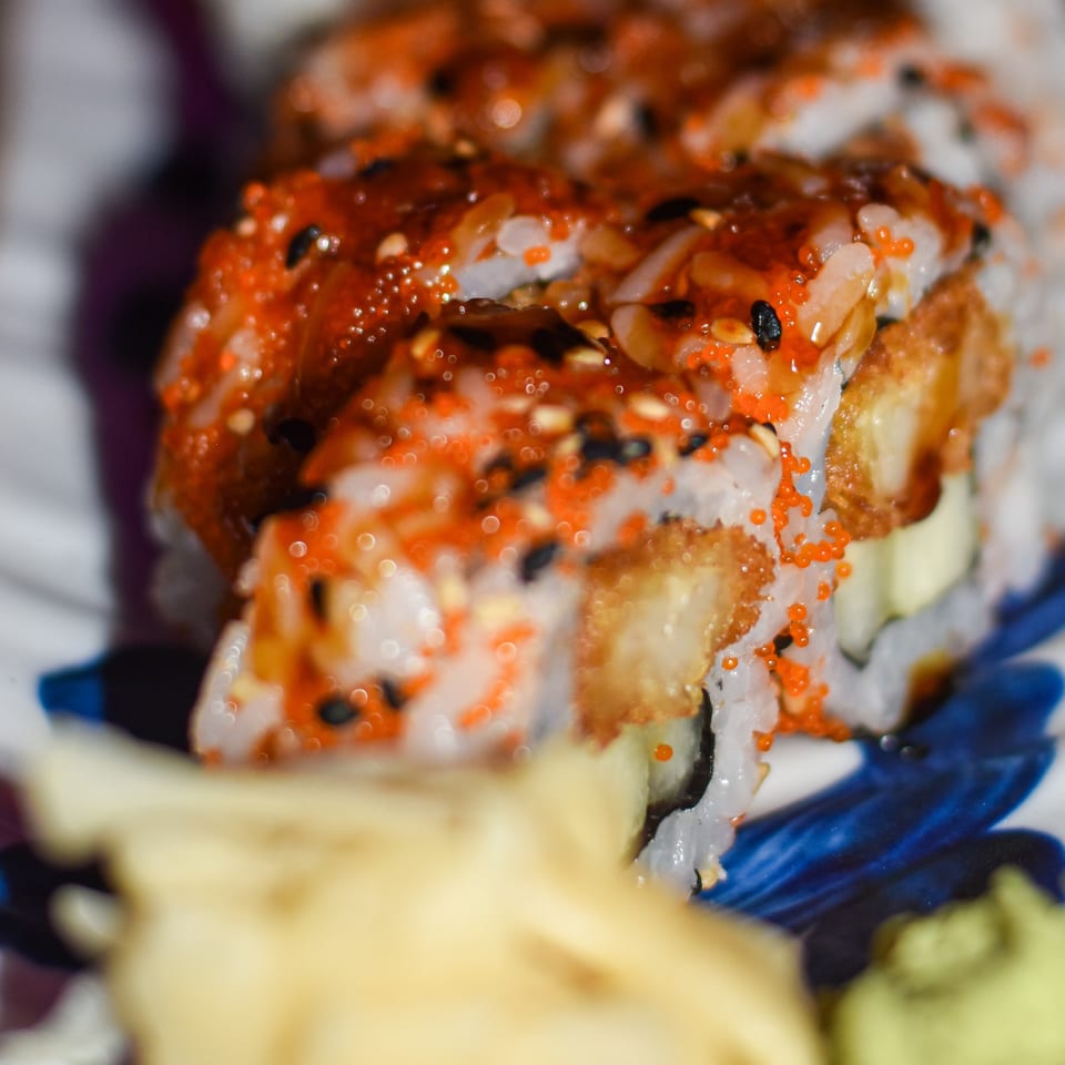 Close-up of assorted sushi rolls topped with orange fish roe, sesame seeds, and sauces on a plate.