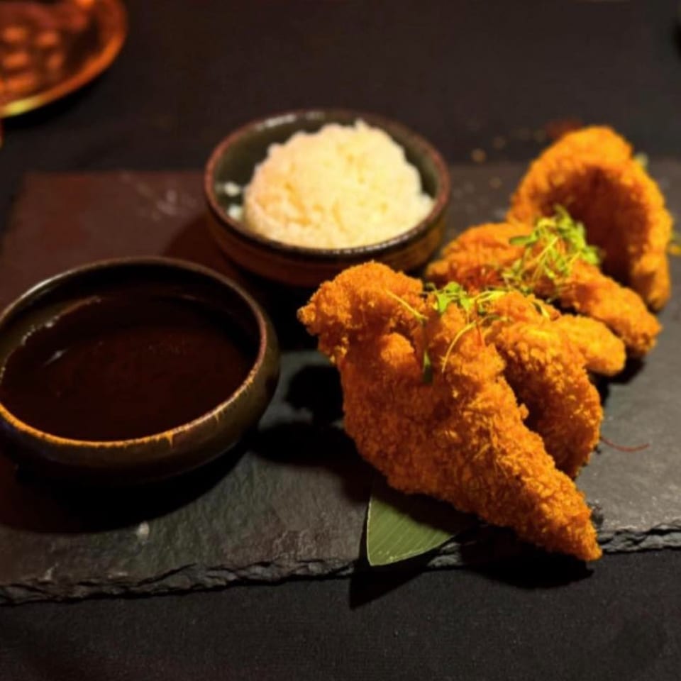 Crispy fried shrimp with microgreens, dipping sauce, and a bowl of creamy rice on a dark slate plate.