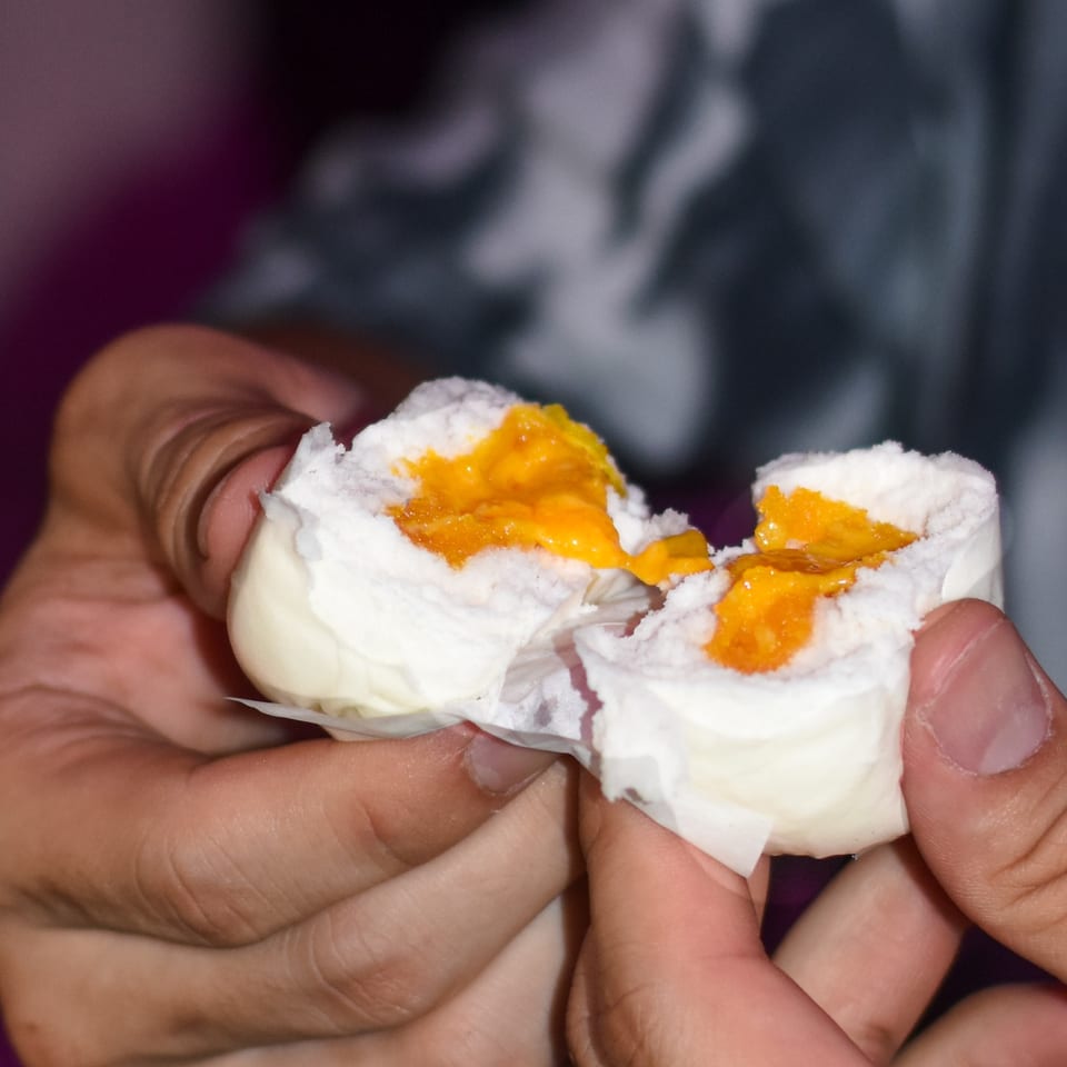 Hands hold a split cream-filled pastry with bright orange fruit filling against a dark background.