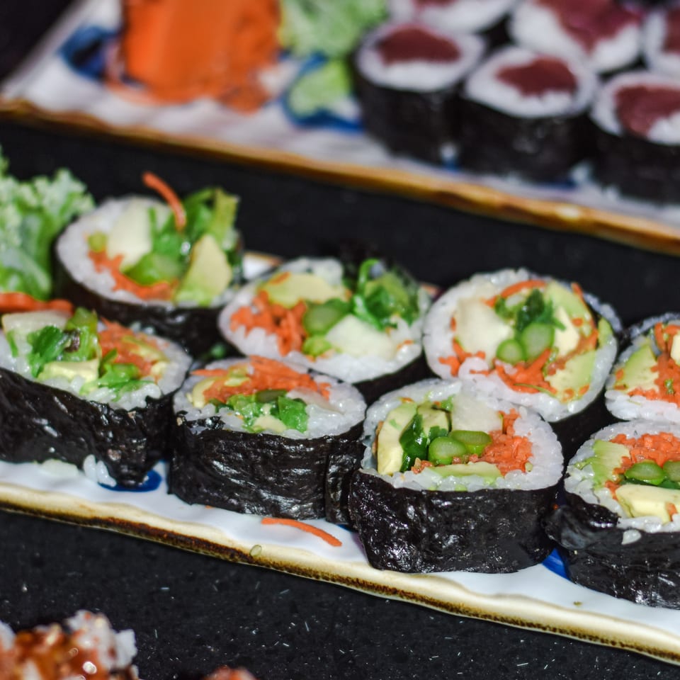 Close-up of assorted sushi rolls filled with rice, avocado, vegetables, and orange roe on rectangular plates.