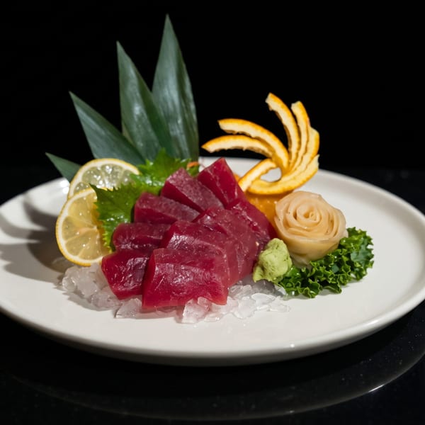 Tuna sashimi on ice with lemon, ginger, wasabi, and orange peel on a white plate.