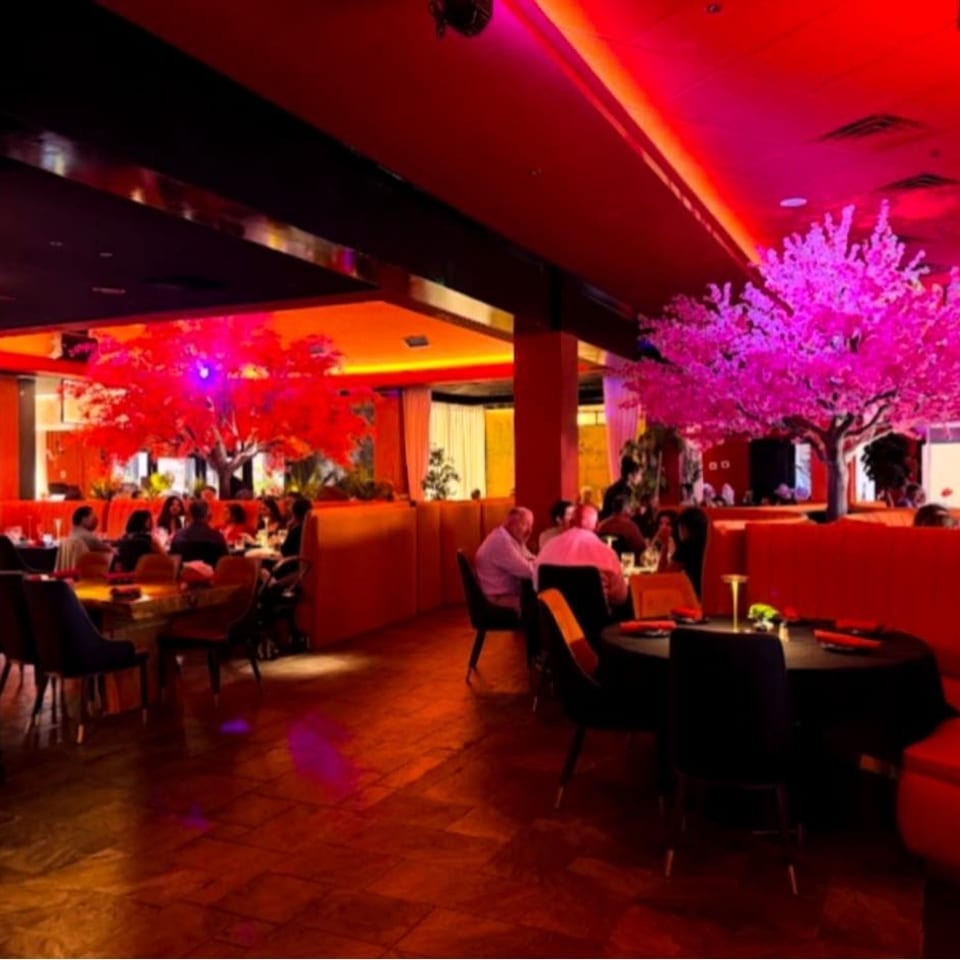Vibrant restaurant dining room with red booths, black tables, diners, mirrored walls, and illuminated pink and red ornamental trees.