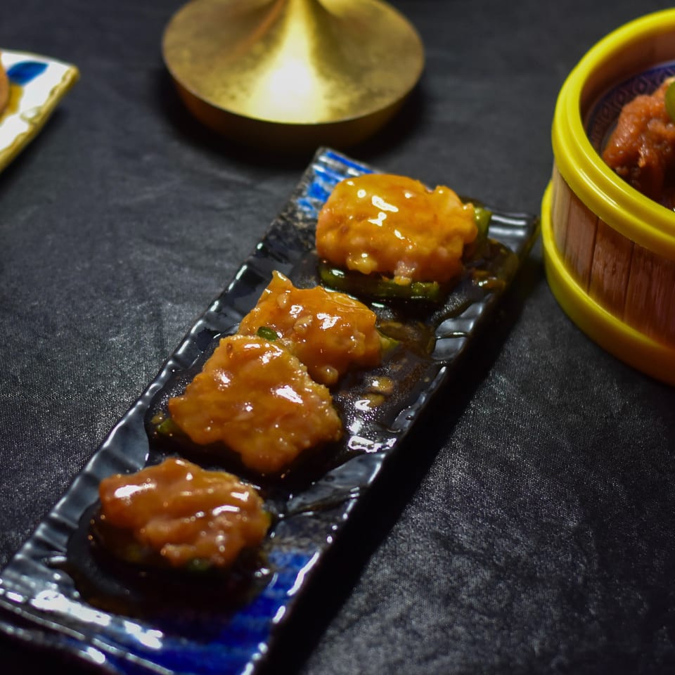 Glazed fried appetizers arranged on decorative plates, with jalapeño-topped bites and spicy chicken pieces in a yellow-rimmed bowl.