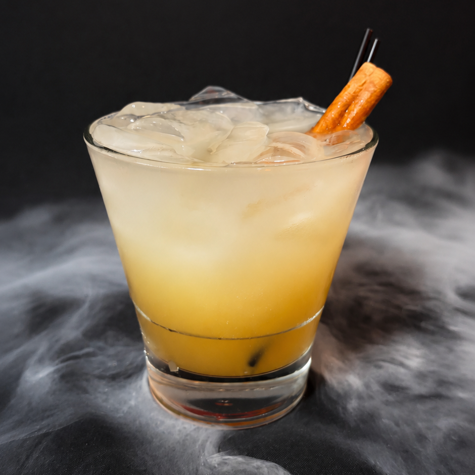 Golden cocktail served over ice in a rocks glass, garnished with an orange twist, surrounded by swirling mist.