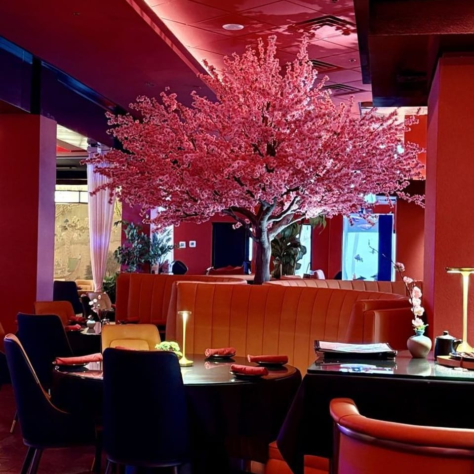 Elegant red restaurant dining room with a large pink blossom tree, leather booths, and neatly set tables.