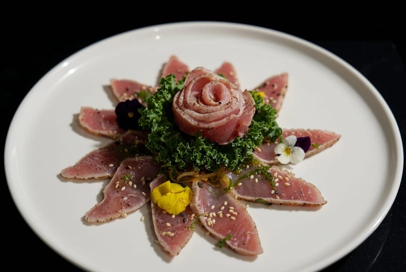 Seared tuna sashimi arranged in a flower shape with a tuna rose, kale, and edible flowers.