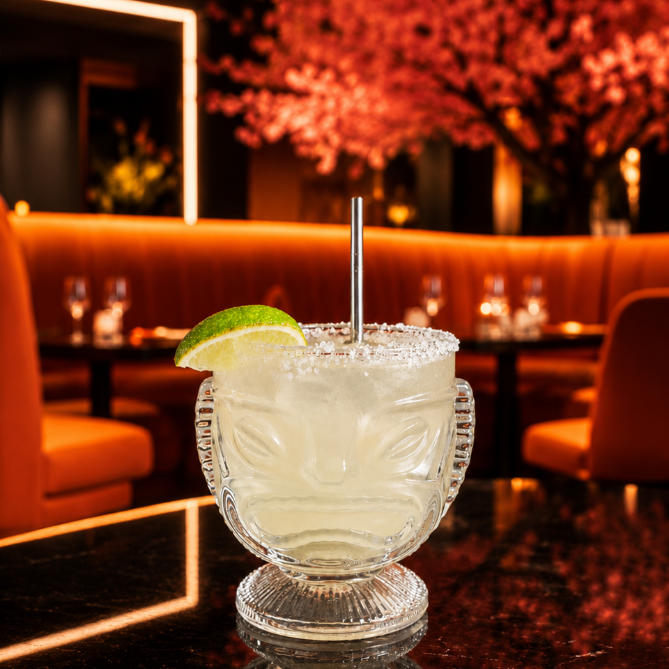 Salt-rimmed margarita with lime wedge in a sculpted glass, presented on a reflective table in a warmly lit restaurant lounge.